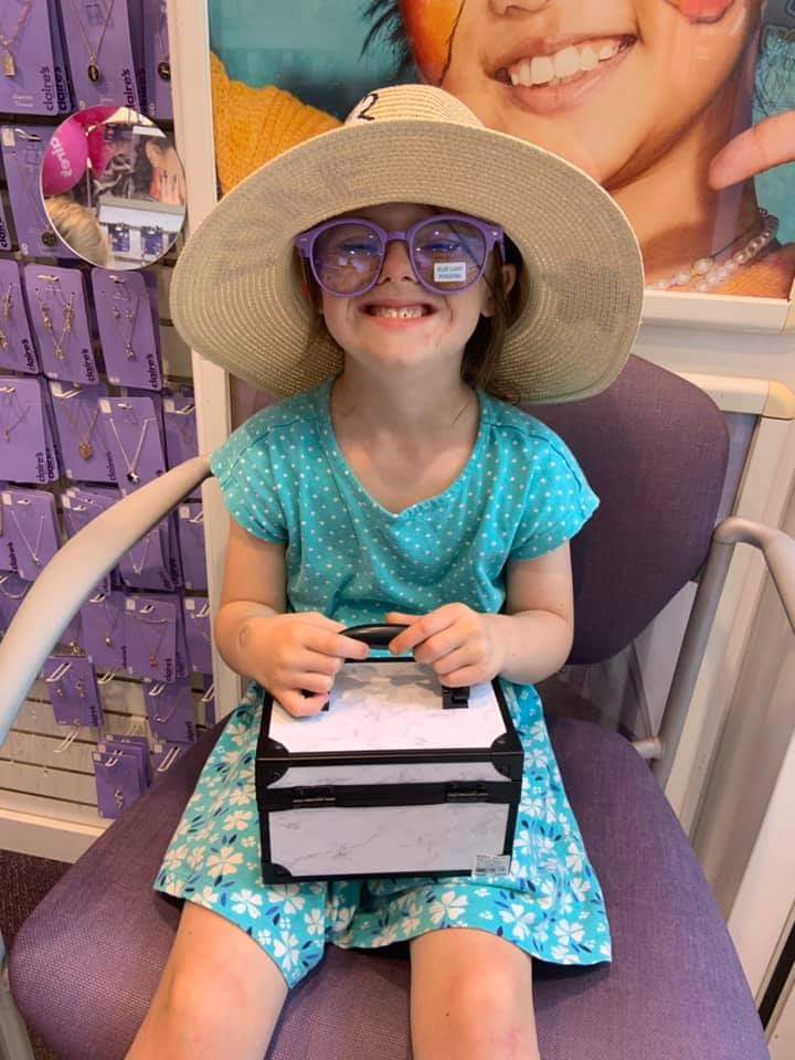 Young girl with Down syndrome in a blue dress wearing a hat and sunglasses