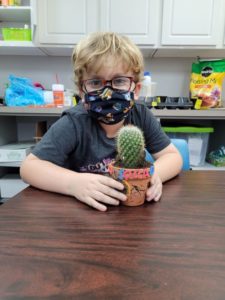 boy with blond hair wearing a face mask and glasses holding a cactus