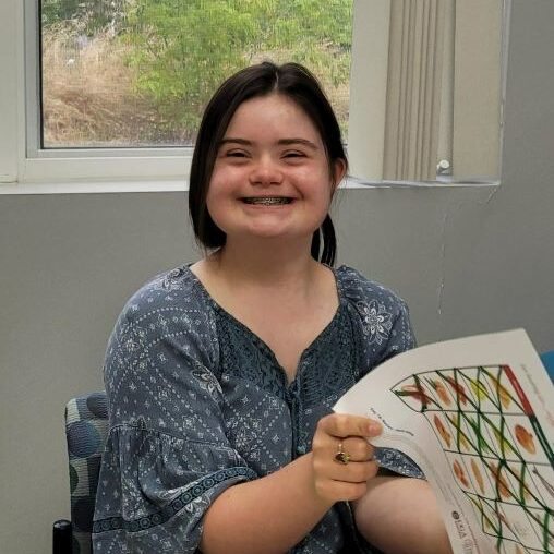Girl with Down syndrome smiling and holding a paper in front of a window