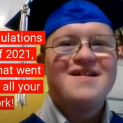 Graduate with Down syndrome wearing a blue graduation cap and smiling