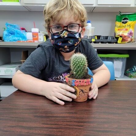 boy with blond hair wearing a face mask and glasses holding a cactus