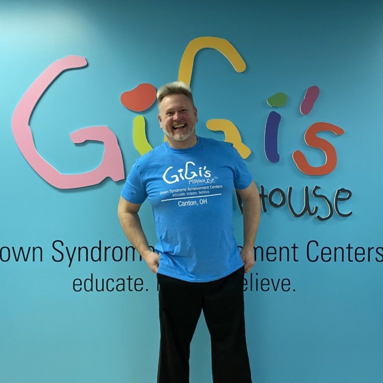 man wearing a blue GiGi's Playhouse shirt in front of a colorful background
