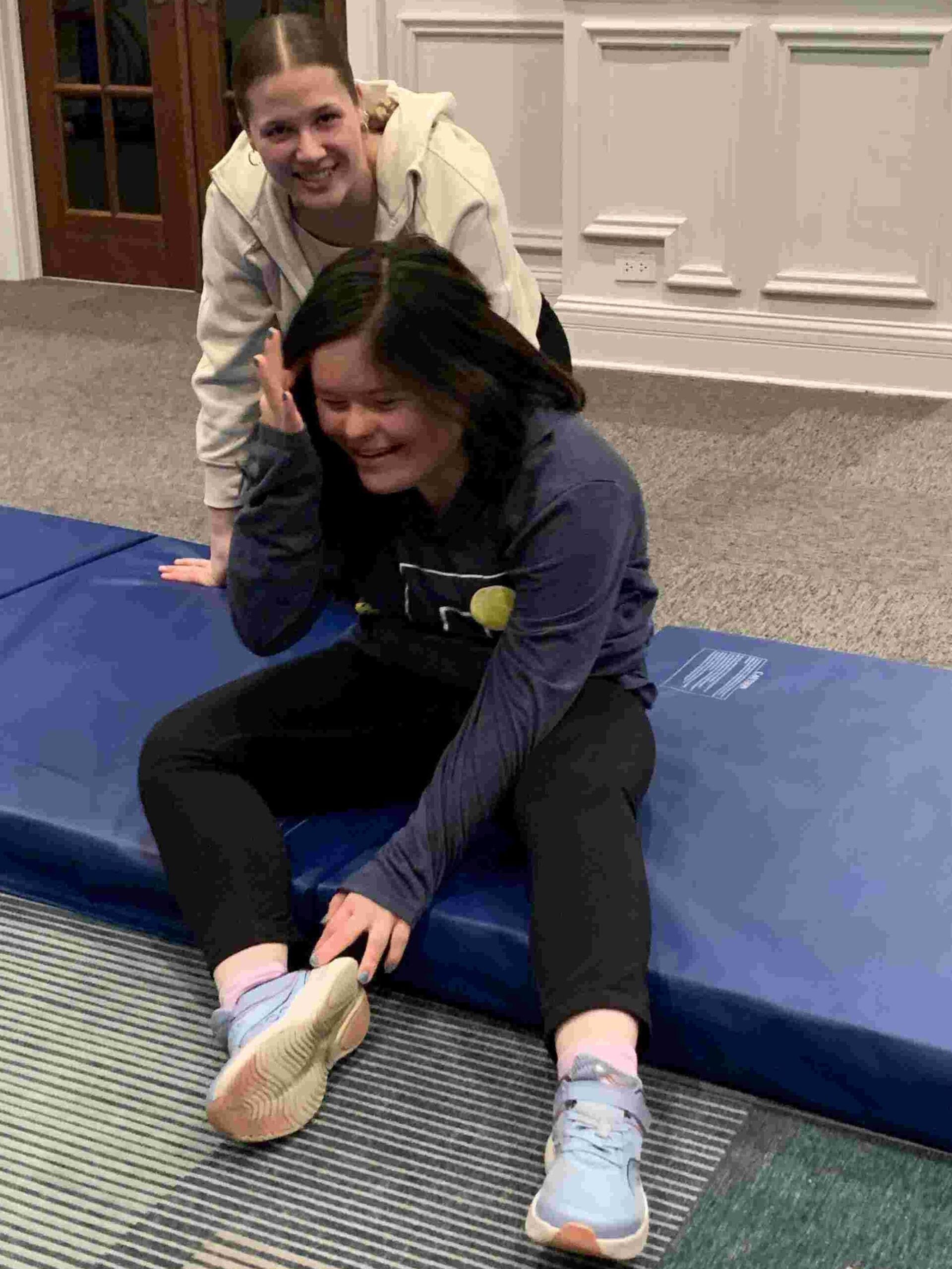Katie a volunteer and Hannah a participant with Down syndrome rest after practicing back bends at dance class