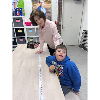 Ian and Sue with a measuring tape showing numbers 1 - 100.