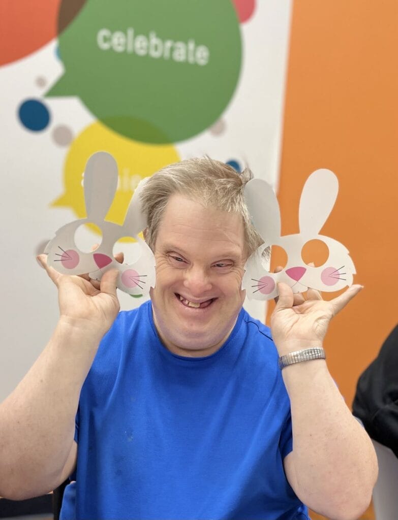 Man smiling while holding two rabbit masks.
