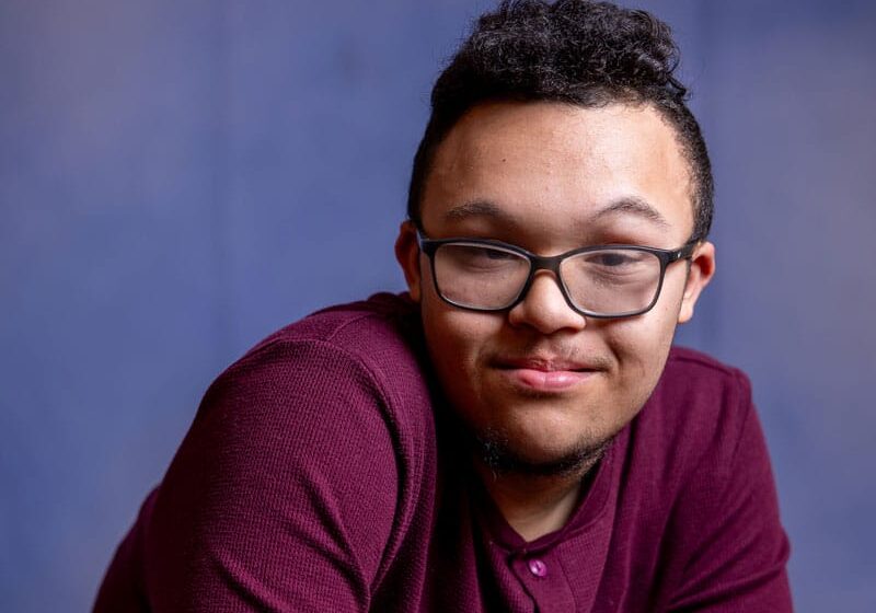 Teenage boy with Down syndrome posing for the camera with a purple background