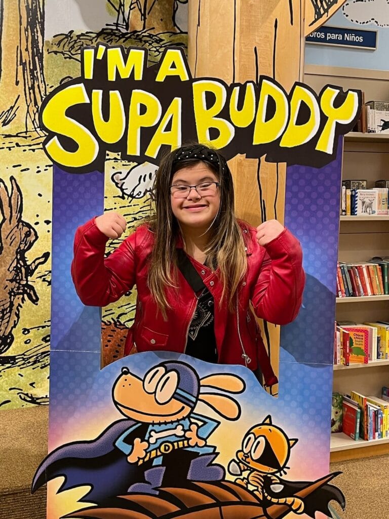 Teenage girl with Down syndrome posing in a sign that says "I'm a Supa Buddy"