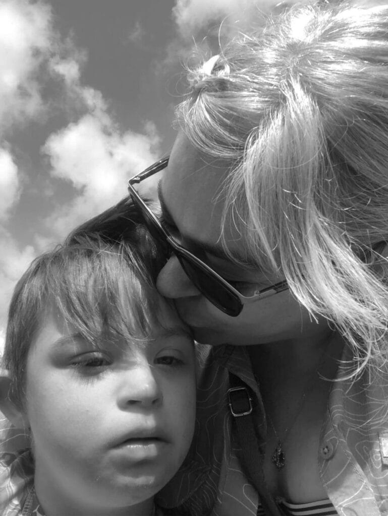 Winchester, young boy with Down syndrome and his mom, Michelle in a black and white photo. Mom is giving her son a kiss on the head.

