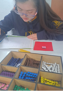 girl in a blue hoodie writing on a work book on table