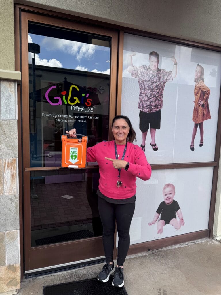 Site Manager, Suzanne Scott, proudly displaying the new AED machine for GiGi's Playhouse Orange County, generously donated from Gable Heart Beats Foundation.