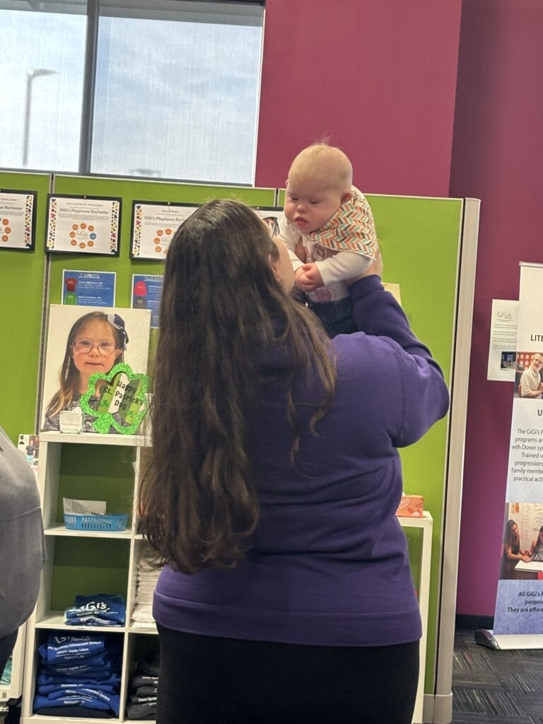 Girl shown from behind, holding up a small child with Down syndrome
