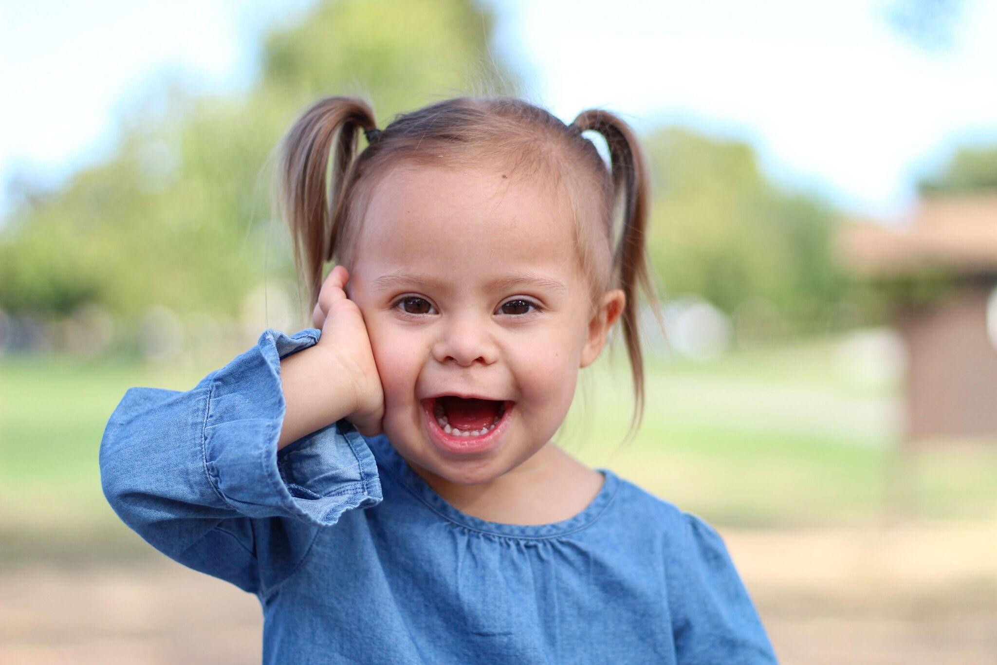 Girl with Down syndrome smiling with her hand on her cheek