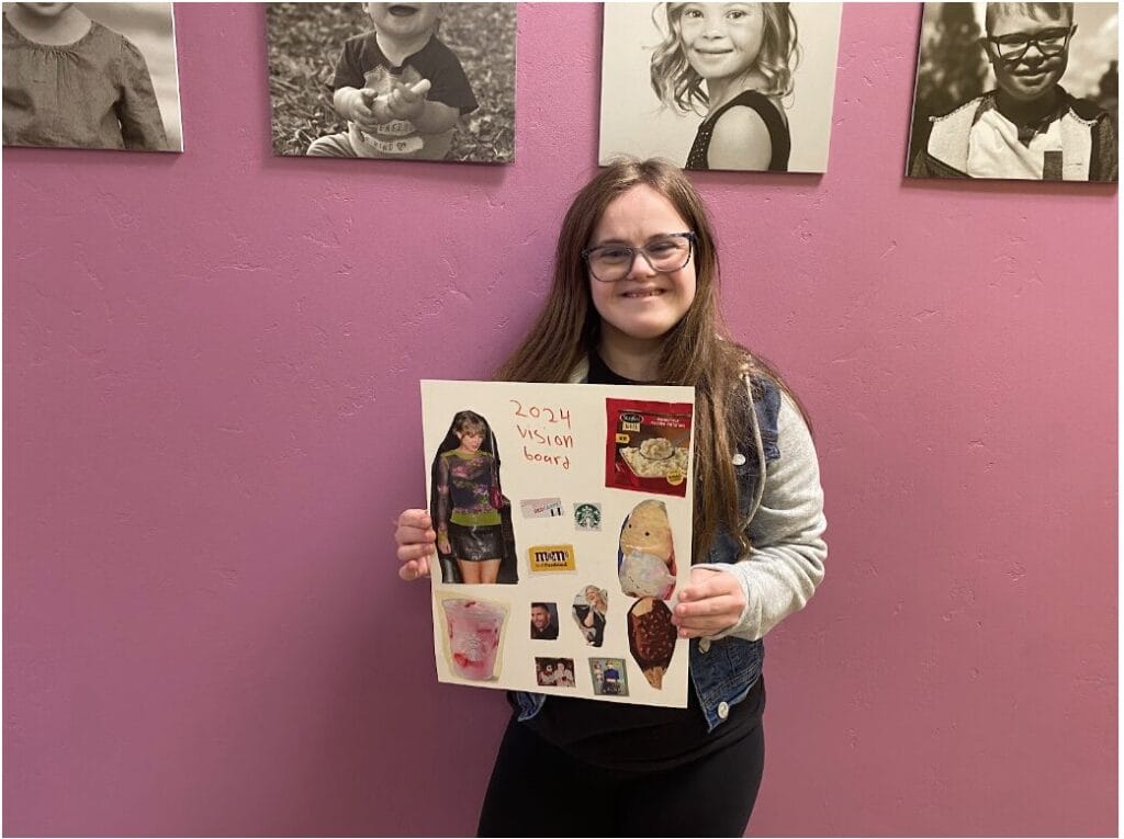 Mia poses with her vision board for 2024 and smiles at the camera