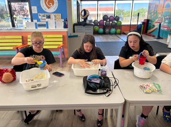three girls sitting at a table making sand as a summer activity