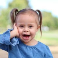 Girl with Down syndrome smiling with her hand on her cheek