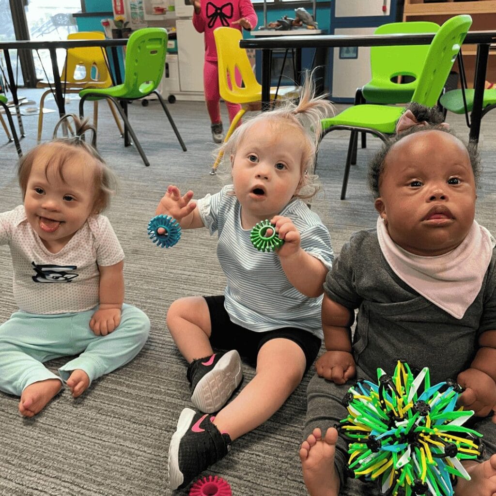 3 babies playing with toys and smiling for a photo.