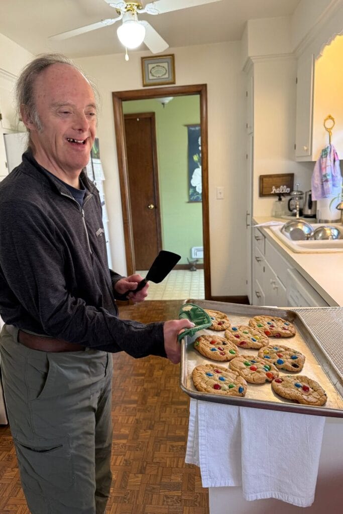 John smiling holding a cookie sheet of perfectly baked M&M cookies