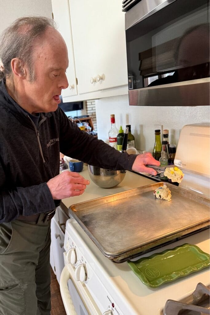 John using a cookie dough scoop to add the cookie dough to the baking sheet