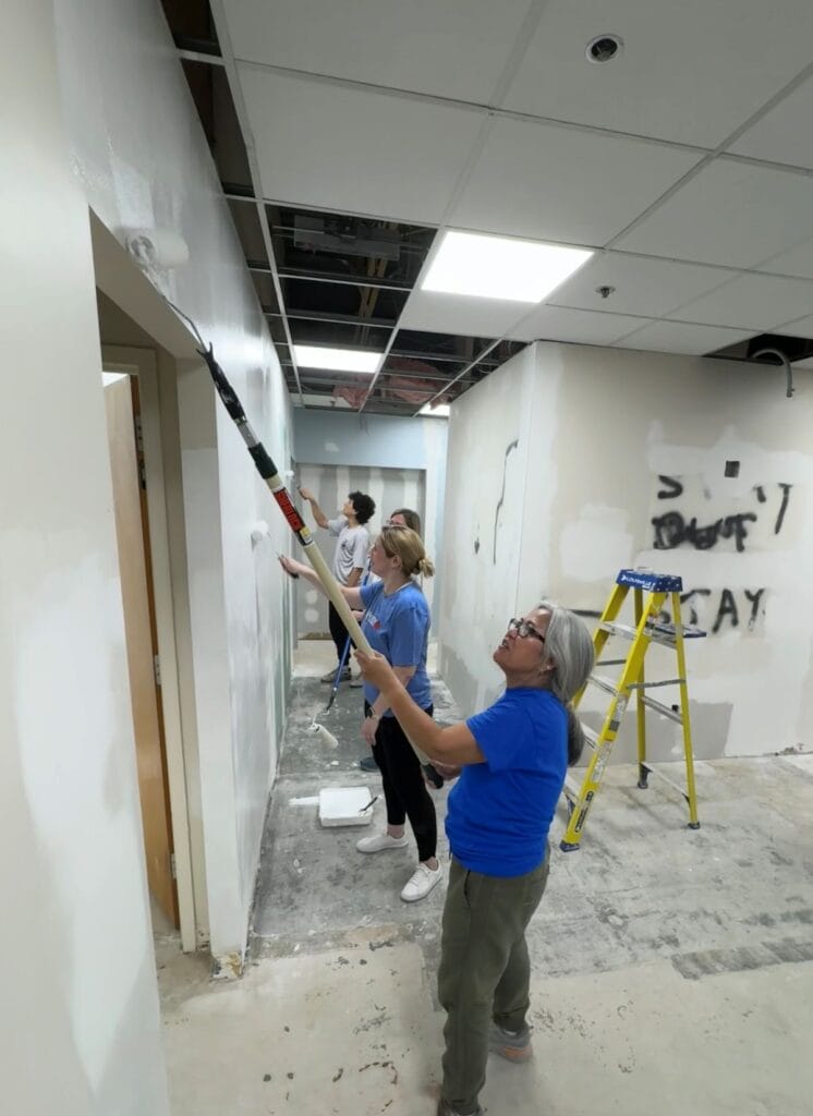 A group of 4 people using roller brushes to paing newly renovated walls.