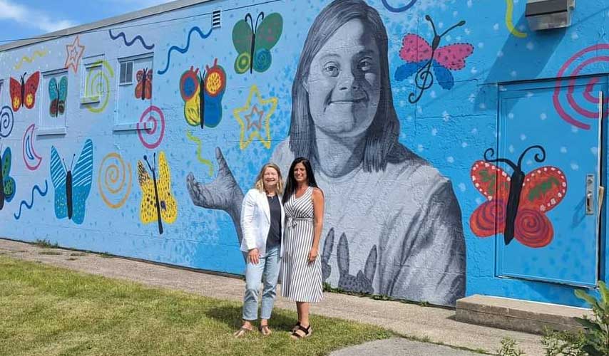 women standing in front of a mural of an individual with Down syndrome