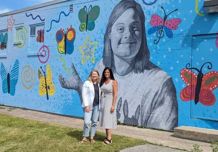 women standing in front of a mural of an individual with Down syndrome